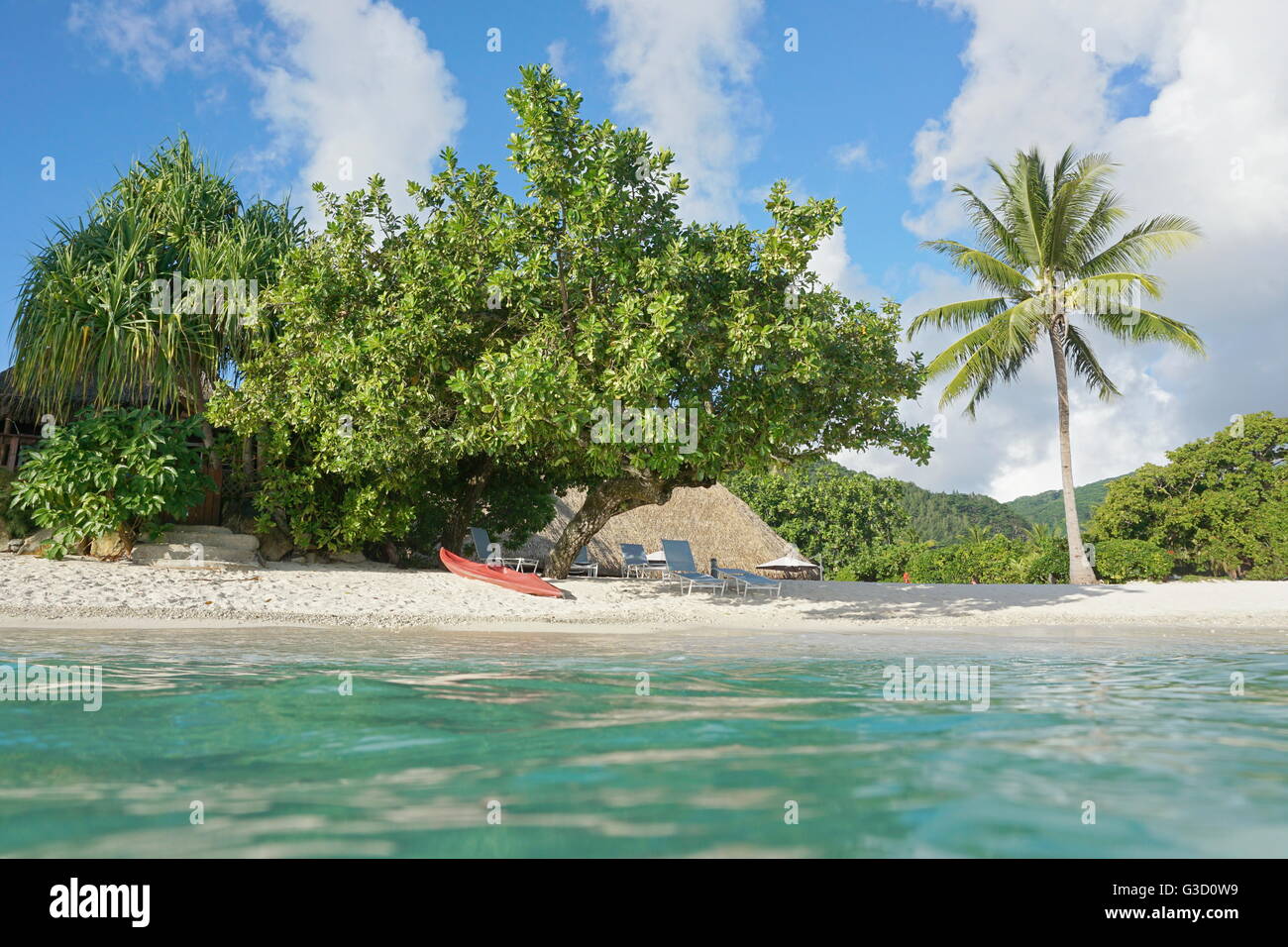 Tropical shore near resort with kayak and lounge chairs on the beach, seen from water surface, Huahine island, French Polynesia Stock Photo