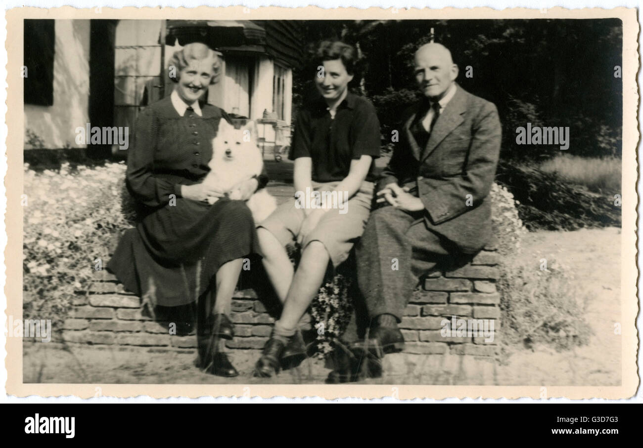 Three people in a garden with a dog Stock Photo - Alamy