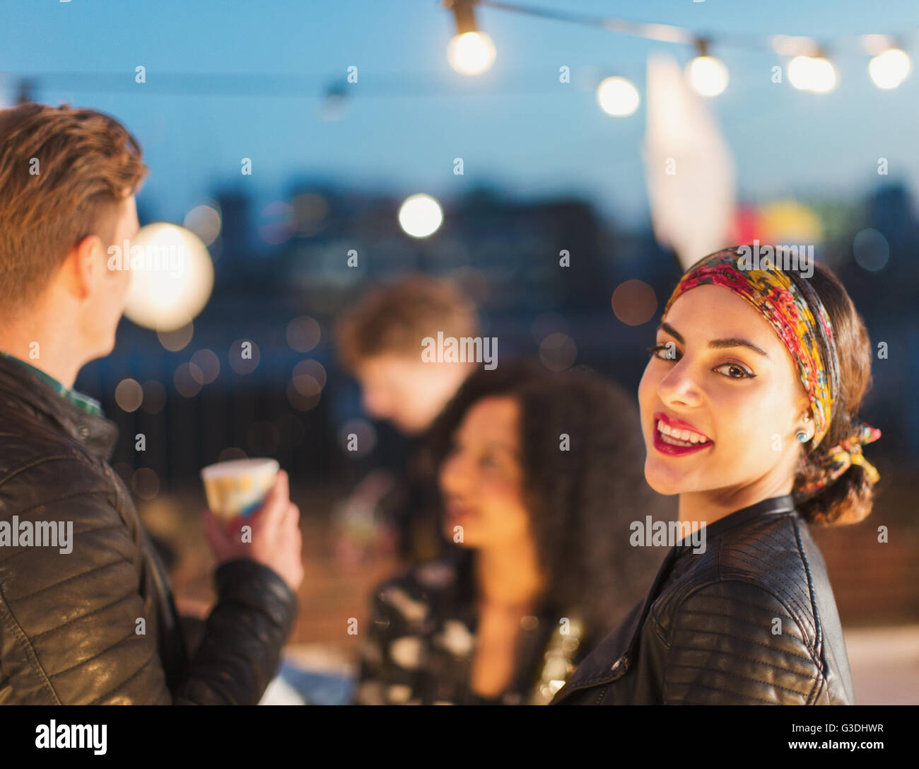 Portrait smiling young woman enjoying rooftop party at night Stock Photo