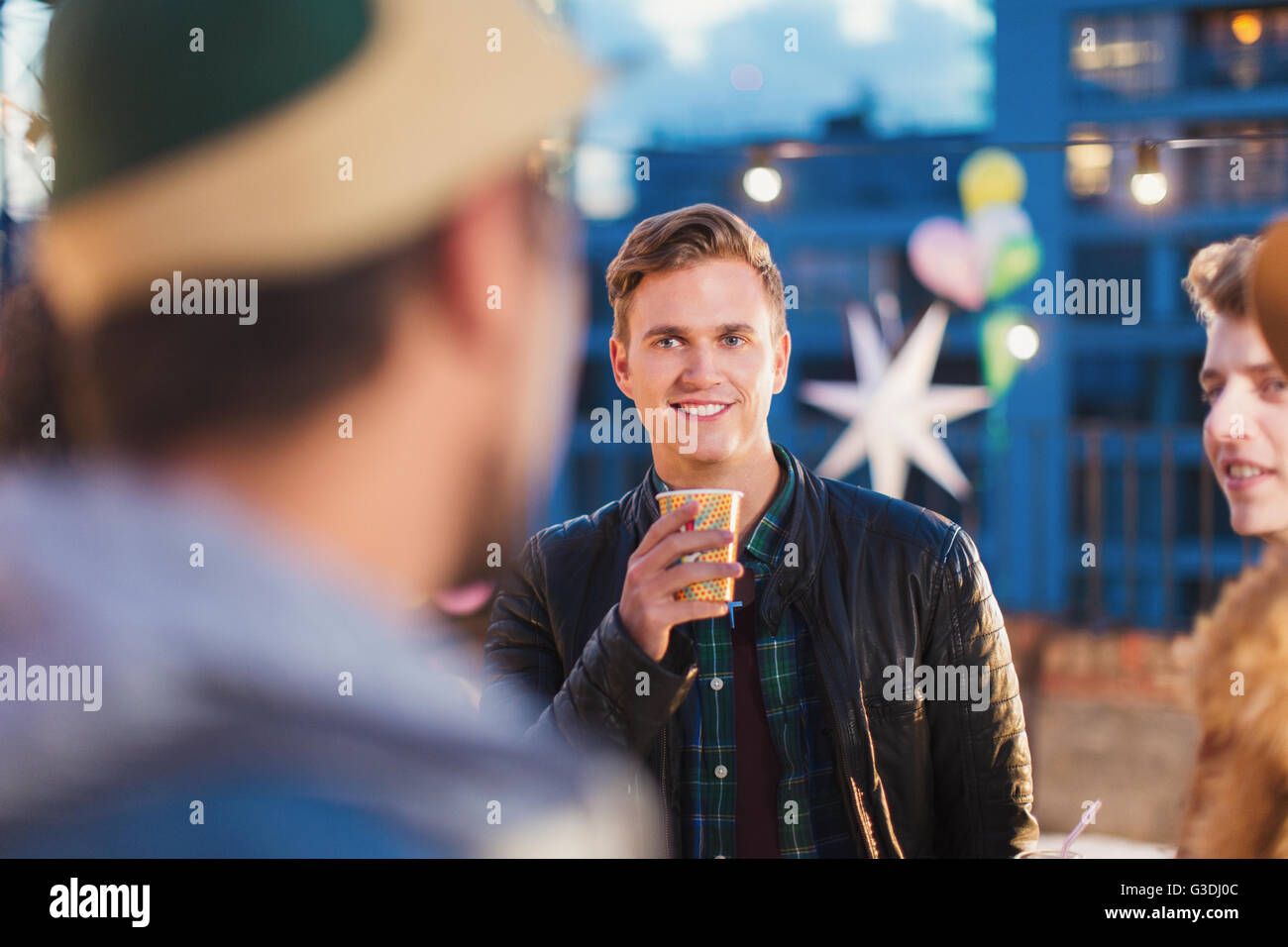 Young adult friends talking and drinking at nighttime rooftop party Stock Photo