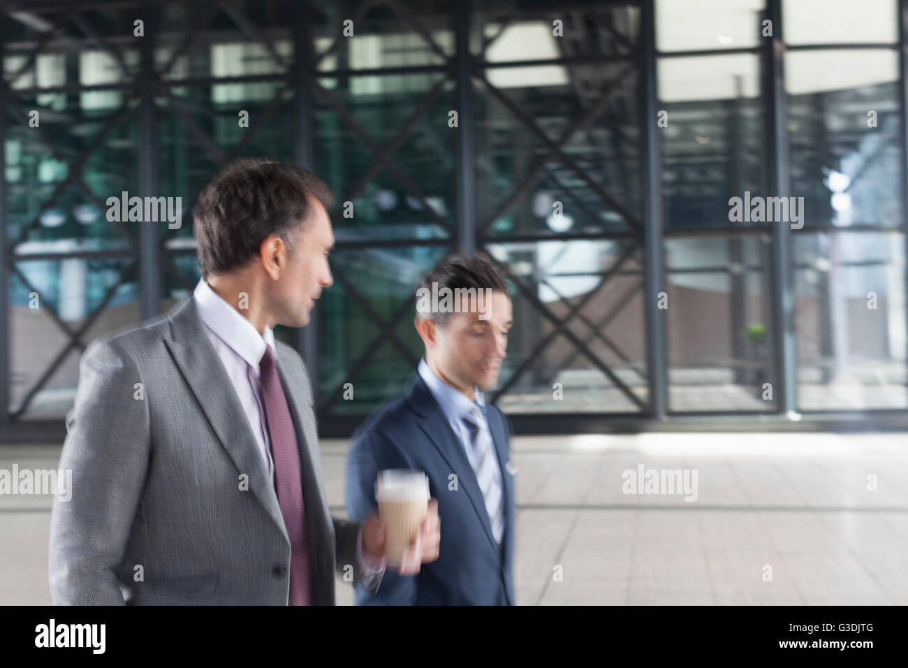 Corporate businessmen with coffee walking and talking outside building Stock Photo