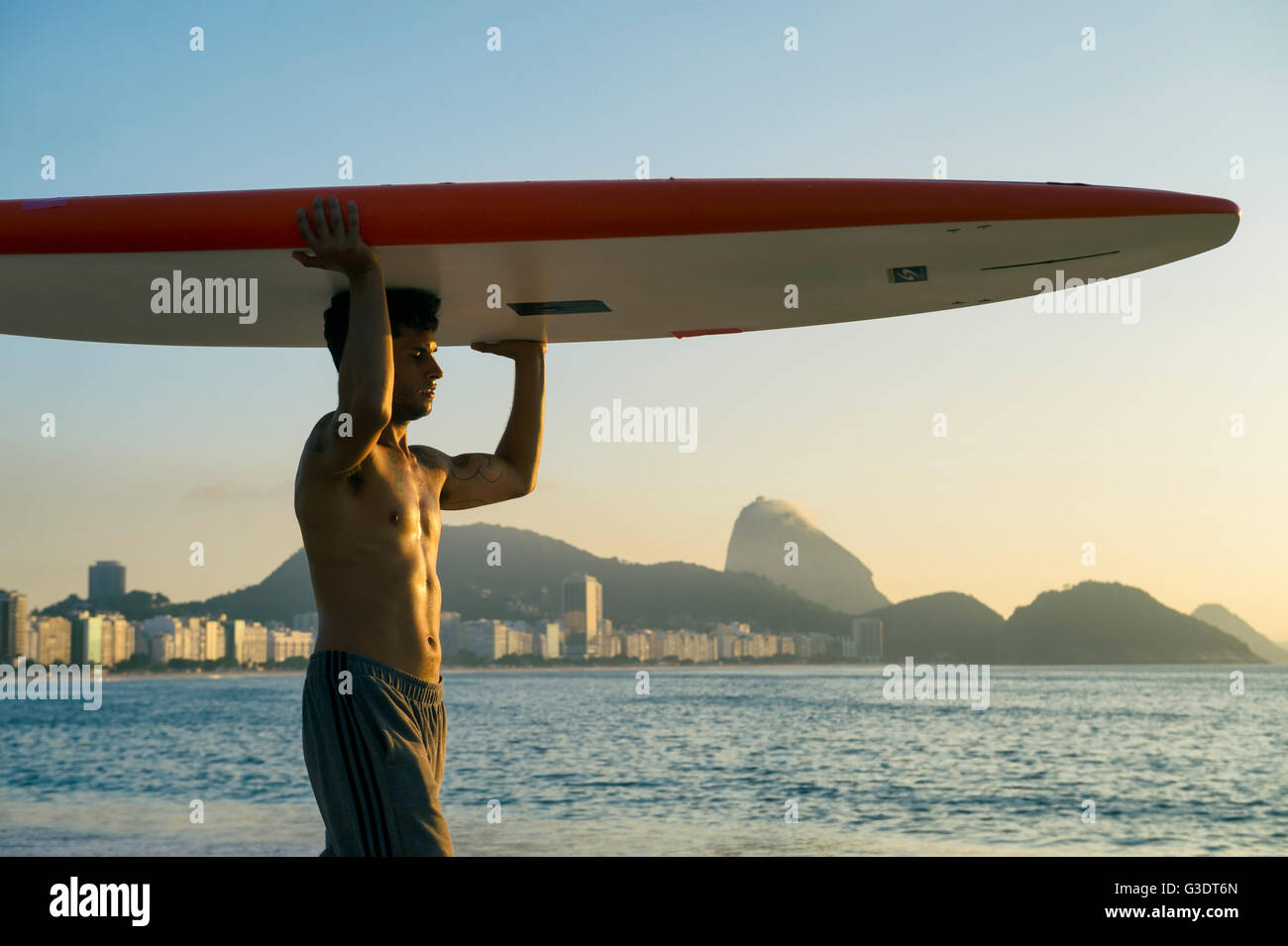 RIO DE JANEIRO - APRIL 5, 2016: A young Brazilian man on Copacabana Beach balances a surfboard in front of Sugarloaf Mountain. Stock Photo