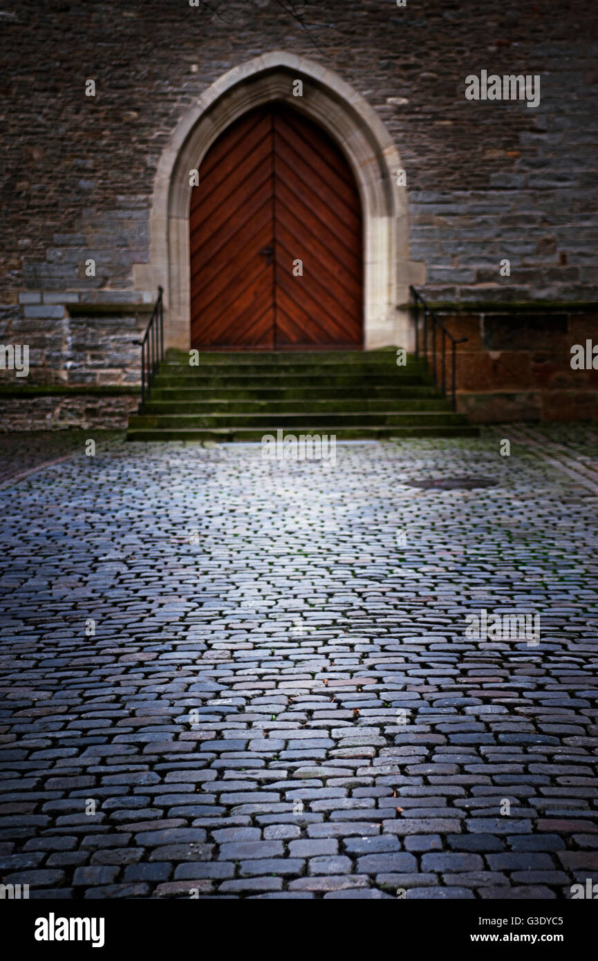 Cobbled courtyard in front of a staircase leading to an old Gothic door Stock Photo