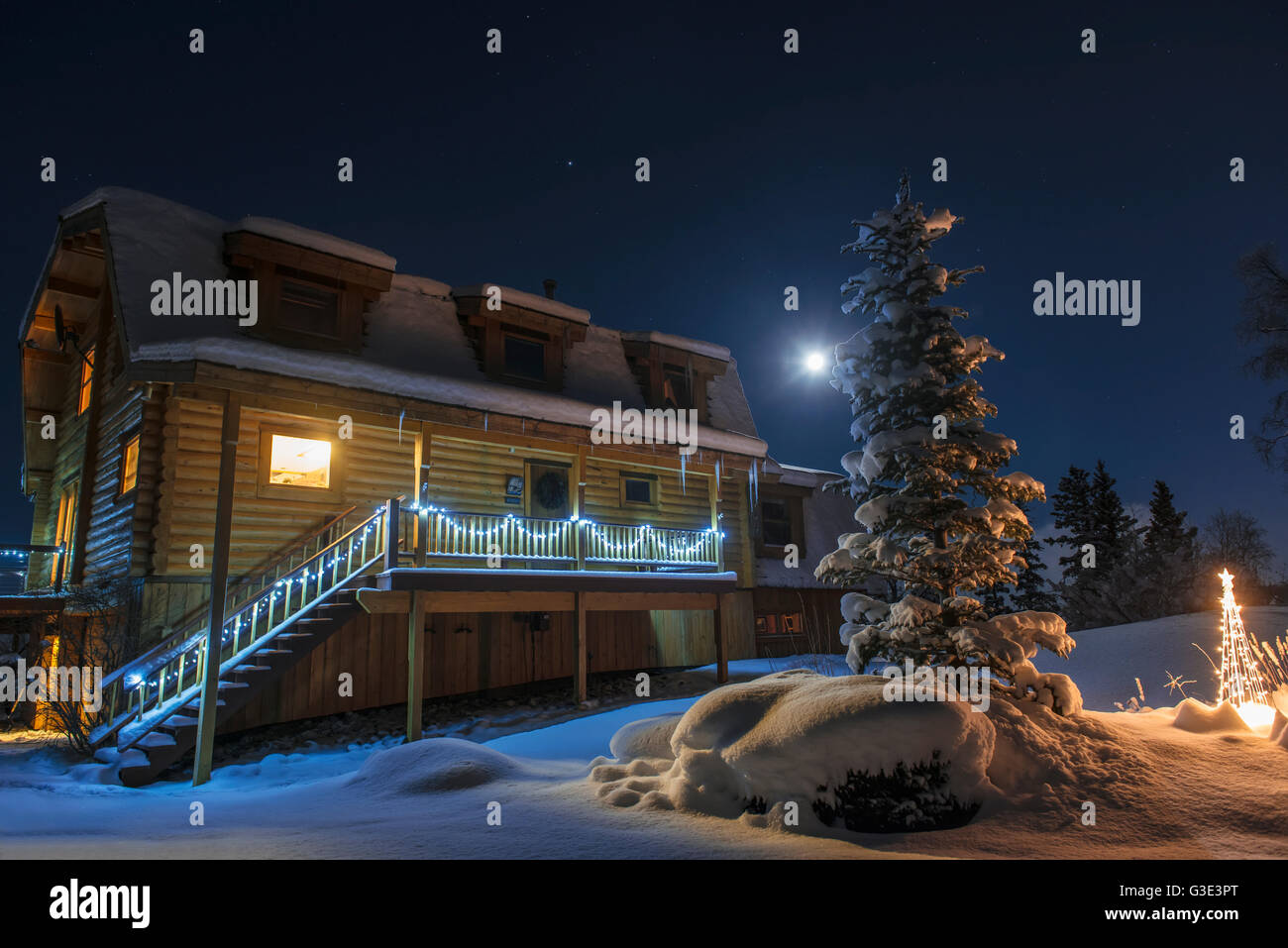 Full moon and holiday lights brighten up a wintery night at a log home in Anchorage, South-central Alaska Stock Photo
