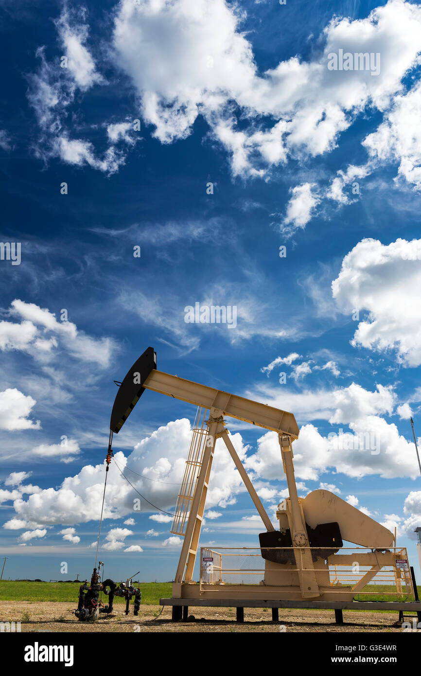 Pump jack in a field with large puffy clouds and blue sky; Alberta