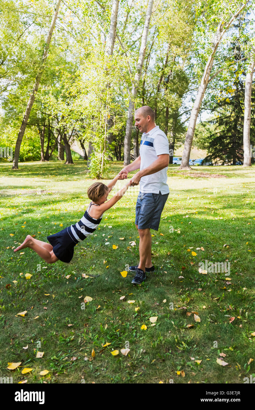 A father swinging his daughter around in a park during a family outing ...