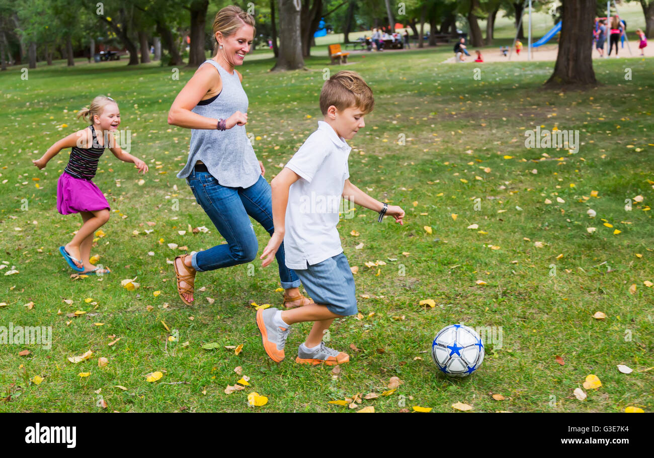 A mother playing soccer with her kids in a park during a family outing