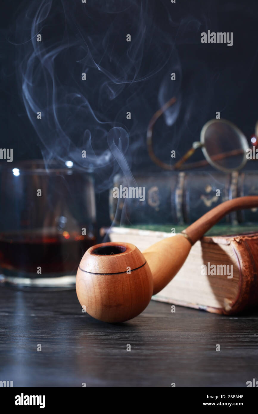 Wooden smoking pipe on old book near glass of alcohol Stock Photo