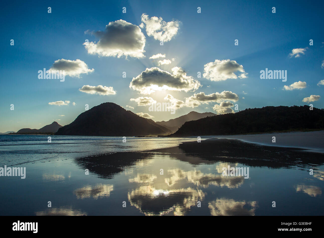 Beautiful ocean sunset. Clouds and sun light reflecting in the water on the beach Stock Photo