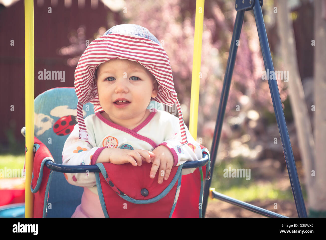 Cute little baby sitting on swings during sunny summer day in the park