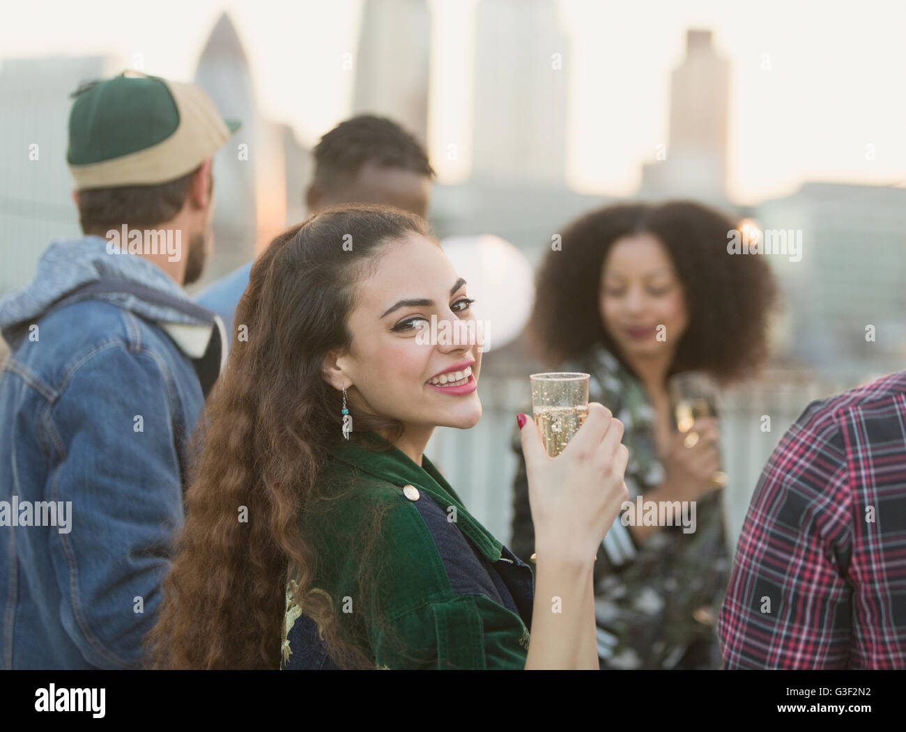 Portrait smiling young woman drinking champagne at rooftop party Stock Photo