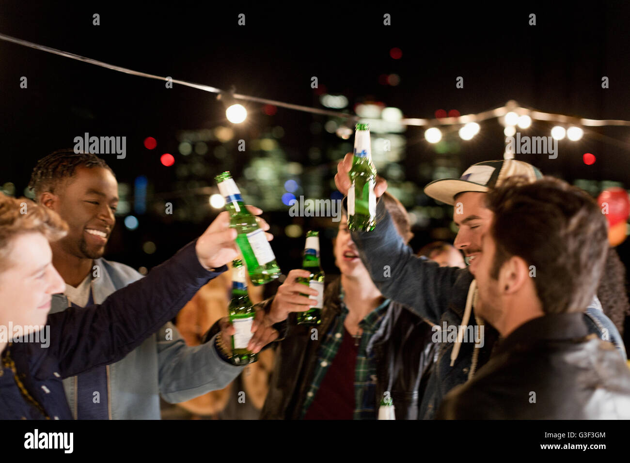Young men drinking beer and dancing at rooftop party Stock Photo