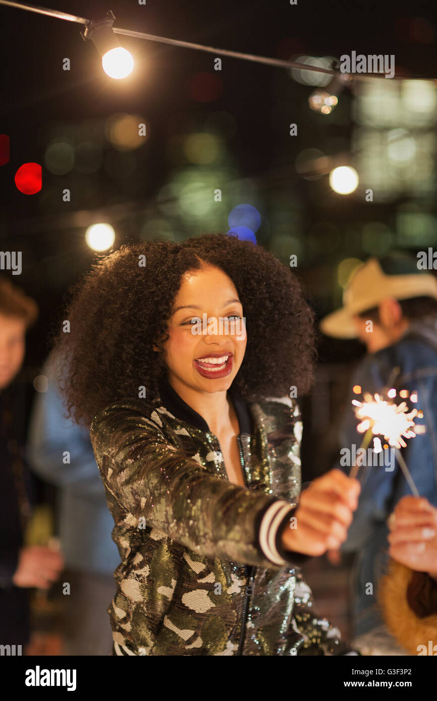 Enthusiastic young woman waving sparkler at rooftop party Stock Photo