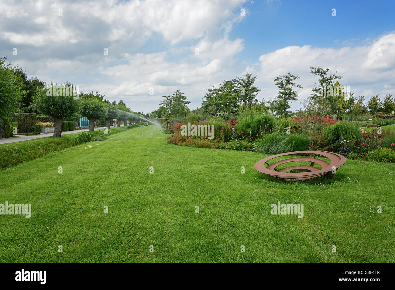 Lawn with a border of flowering plants and an art object. Stock Photo