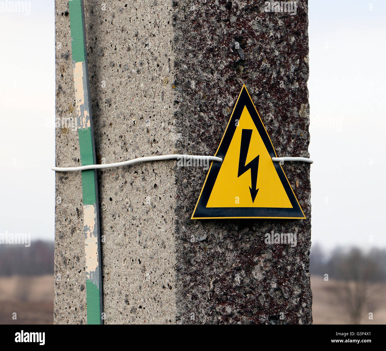 Reinforced concrete electricity pole with sign warning caution electricity shock risk high voltage keep out Stock Photo