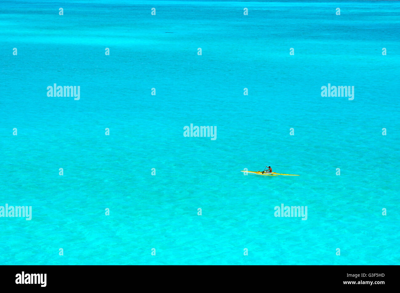 Man paddling in a yellow outrigger canoe in the clear water of the turquoise blue lagoon of Bora Bora island in Polynesia. Stock Photo