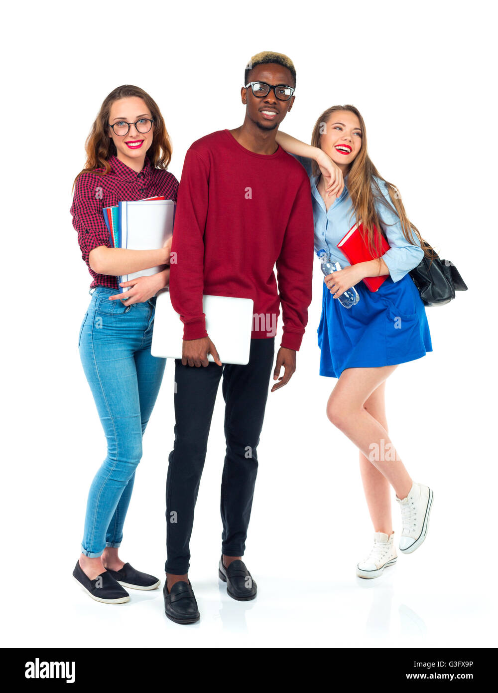 Three happy young teenager students standing and smiling with books, laptop and bags isolated on white background Stock Photo