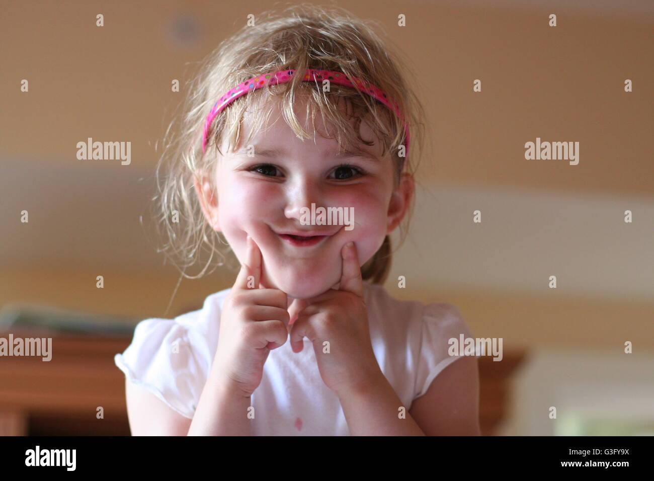 Blonde Little girl child kid having fun playing and messing, making a funny face funny gesture, making a face, pulling faces childhood moment, concept Stock Photo