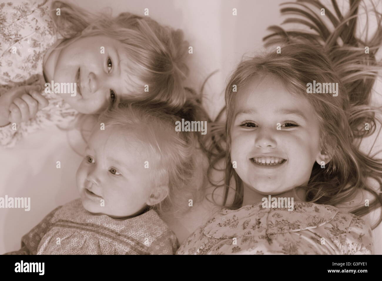 Children, kids lying on the floor laughing and playing together, sepia, family fun, family concept, siblings, little girls, childhood Stock Photo