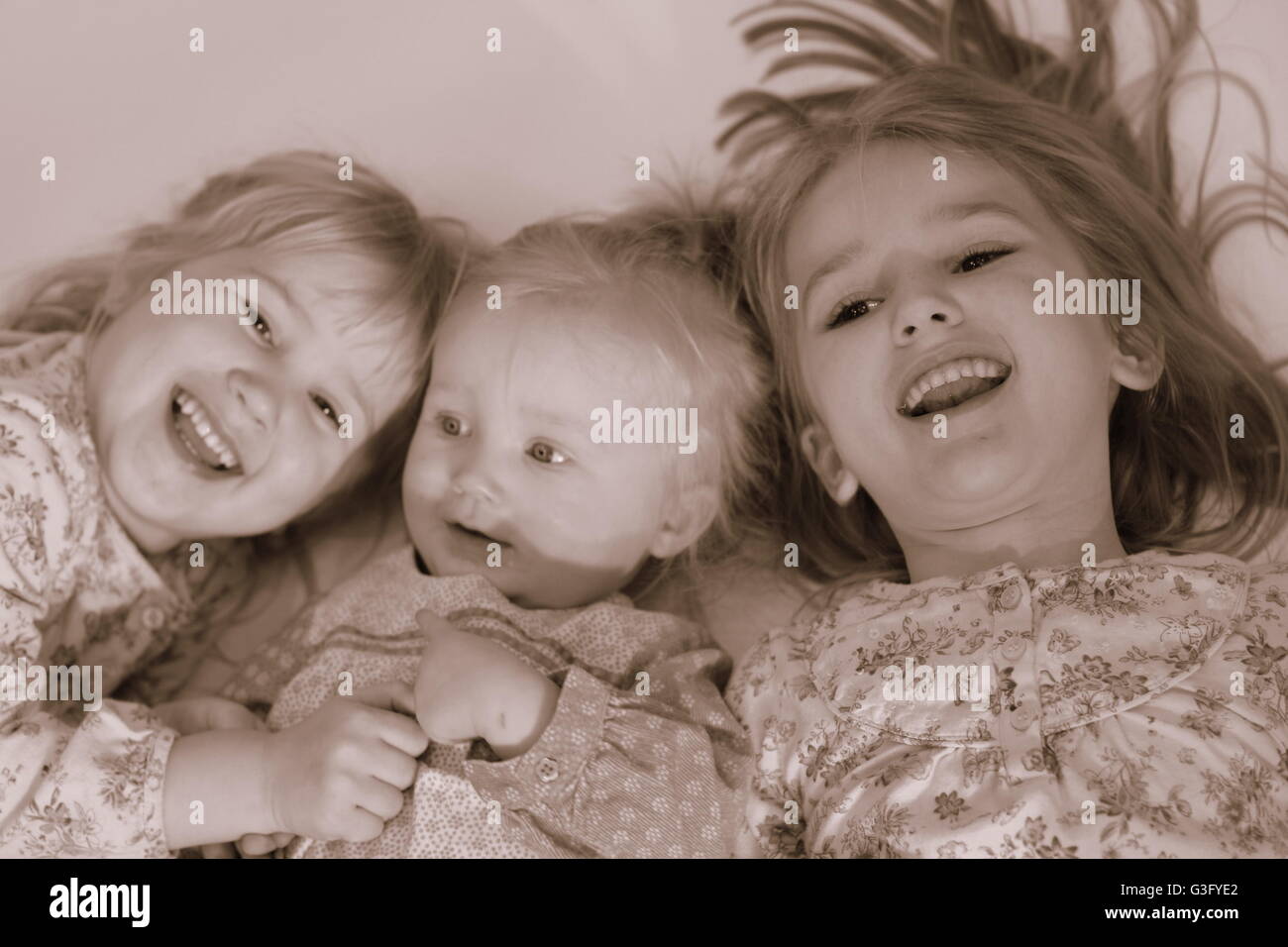 Children, kids, sisters lying on the floor laughing out loud and playing together, sepia Stock Photo