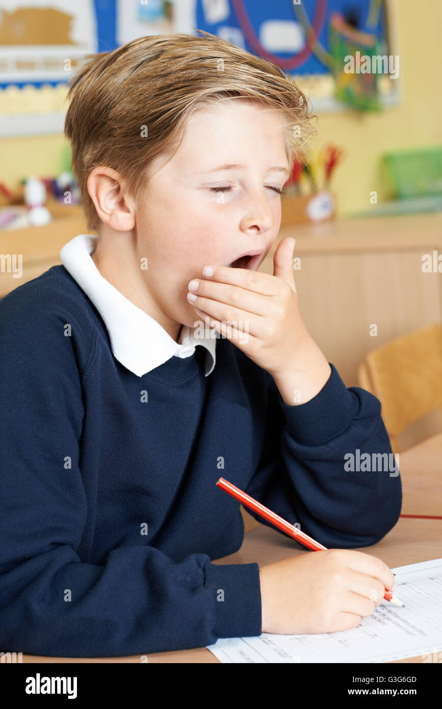 Male Elementary School Pupil Yawning In Classroom Stock Photo