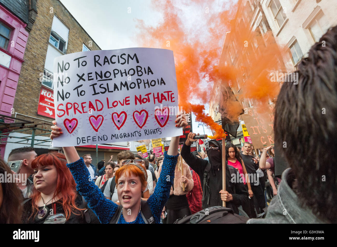 London, UK. June 24th 2016.  A woman holds up a poster in front of flares set off on the long march from Altab Ali Park to the offices of News International on the day after the UK voted to leave the EU. They were protesting against racism, for migrant rights and against fascist violence and argue that migration and immigrants have been attacked and scapegoated not only by both Remain and Leave campaigns but by mainstream parties and media over more than 20 years, stoking up hatred by insisting immigrants are a 'problem'. Peter Marshall/Alamy Live News Stock Photo