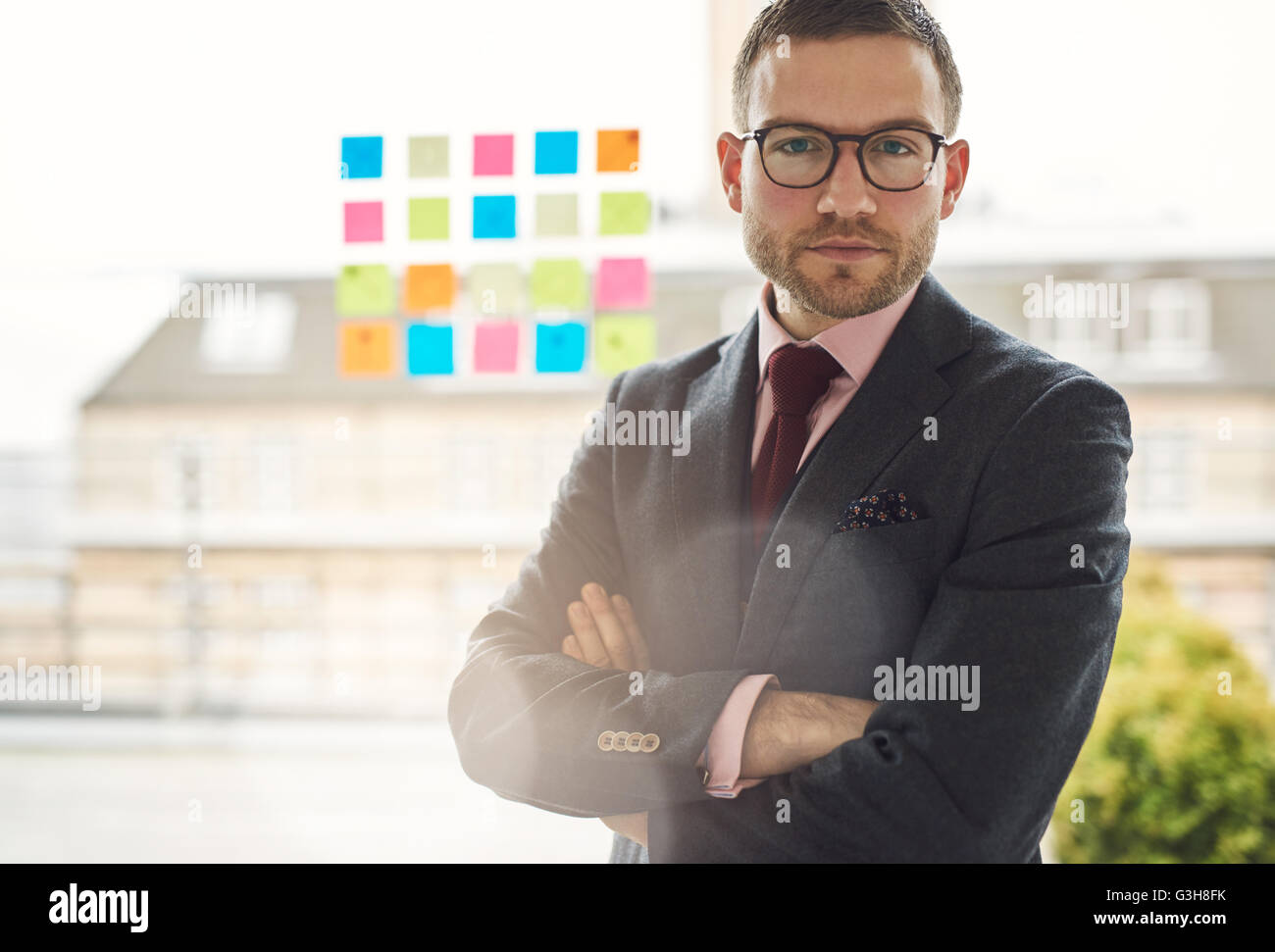 Serious young businessman with crossed arms standing in front of a ...