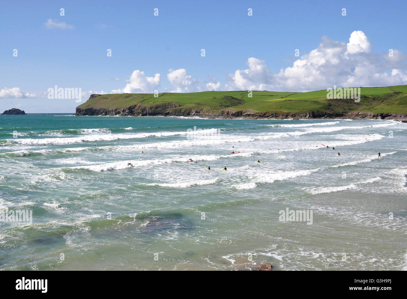 Cornwall - Polzeath beach - surging incoming tide - white capped waves - surfers - backdrop Pentire Head - blue sea and sky Stock Photo