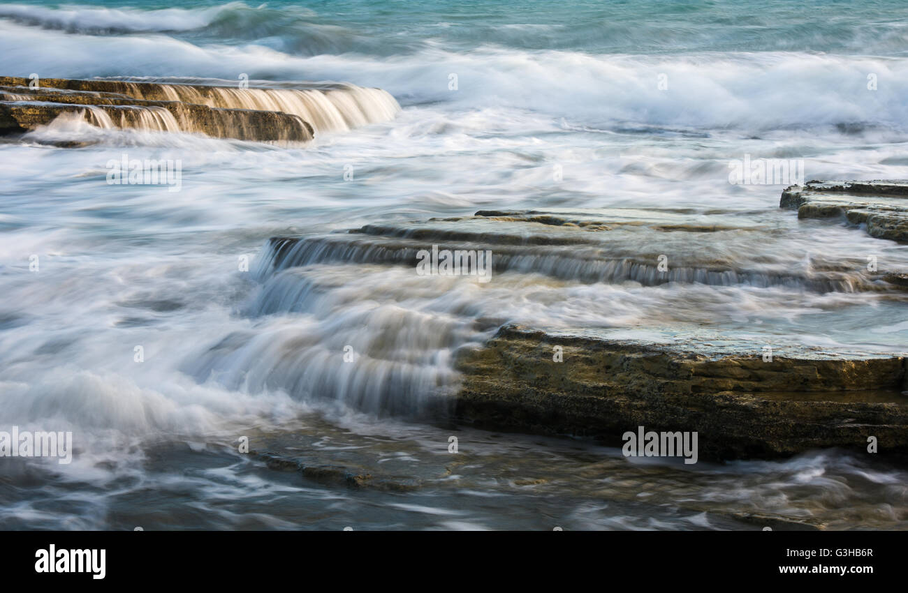 Powerful waves crashing with power on sea rock plates creating small waterfalls and smooth streams of water. Stock Photo