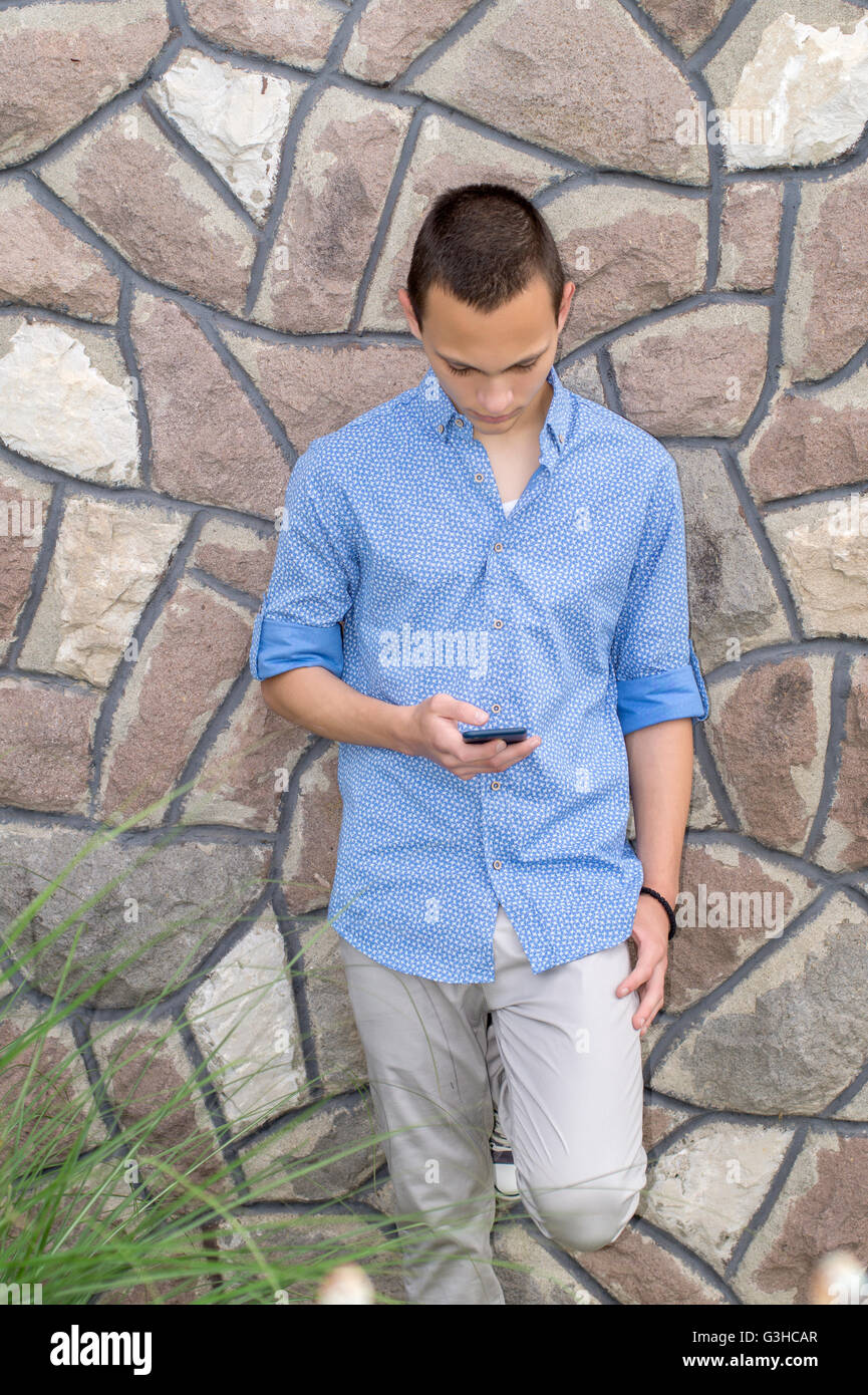 Portrait of cool young man standing against a  wall and reading text message on his cellphone Stock Photo