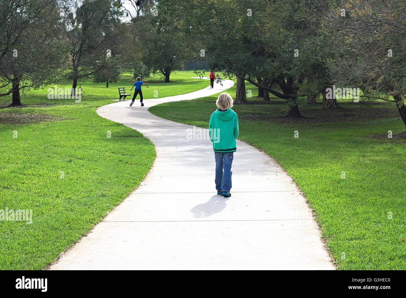 Children skating and walking along a curved concrete path through a