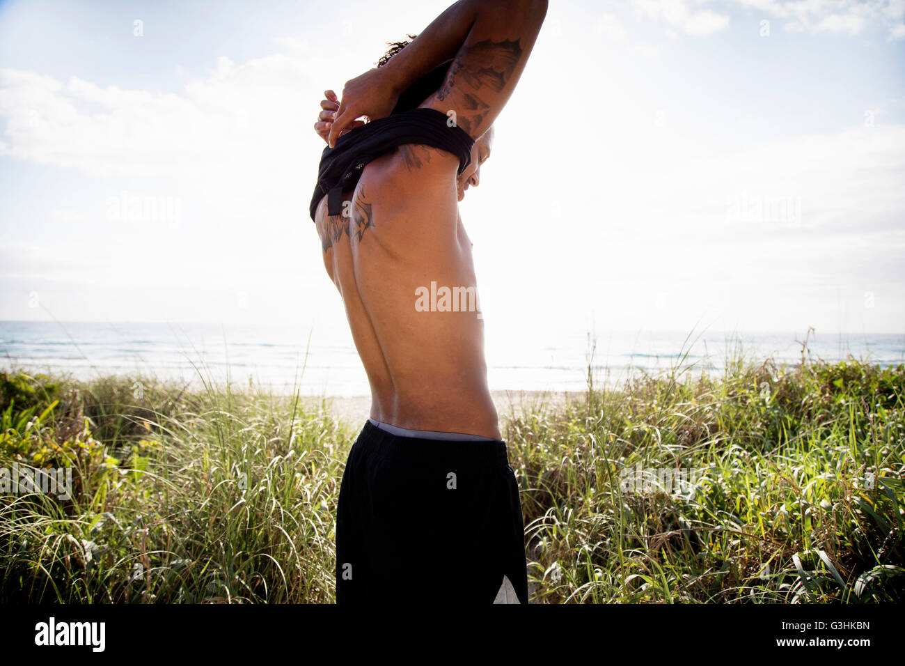 Man removing singlet by ocean Stock Photo