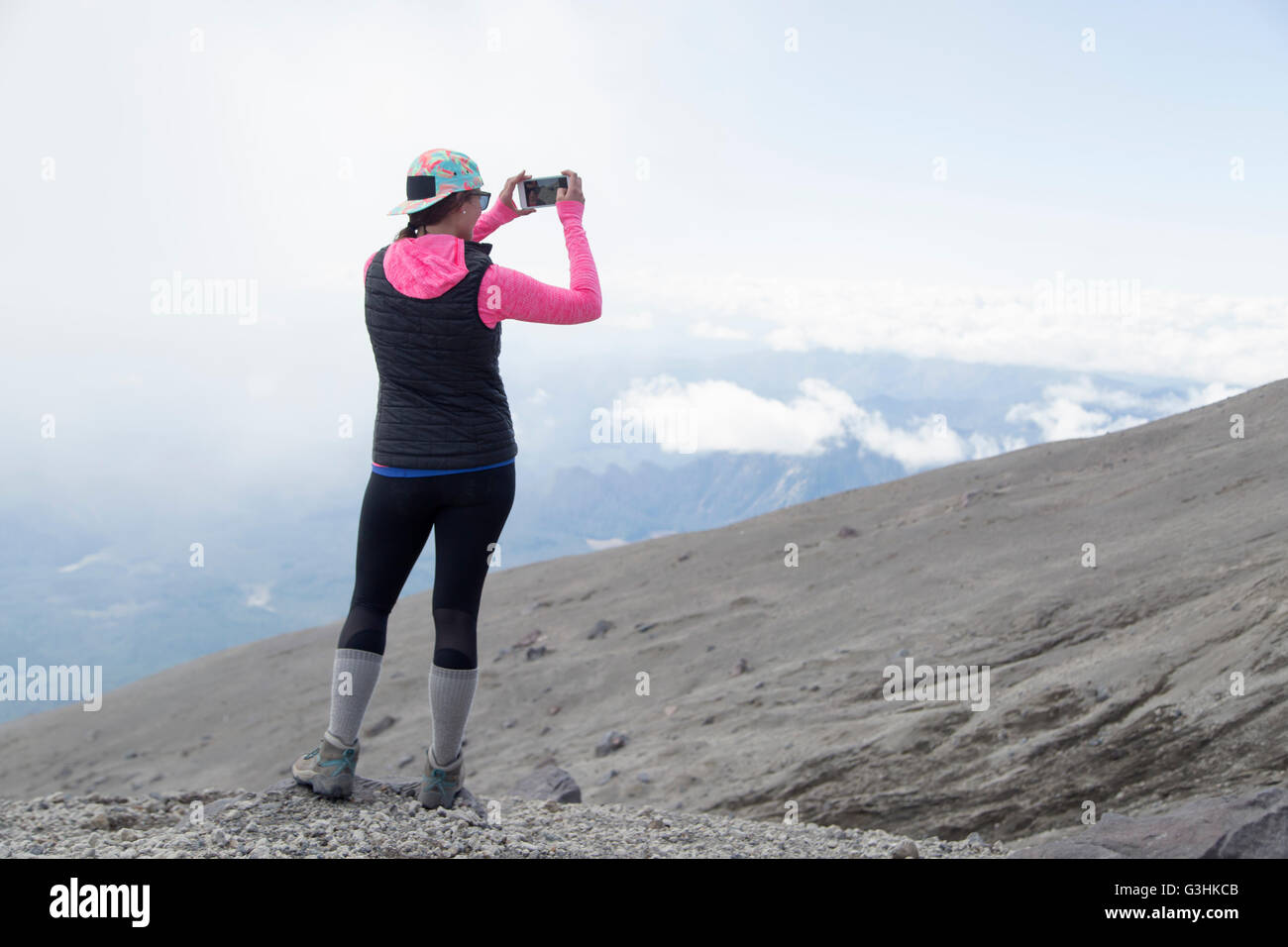 Young woman at mountain top, photographing view, rear view, Mt. St. Helens, Oregon, USA Stock Photo