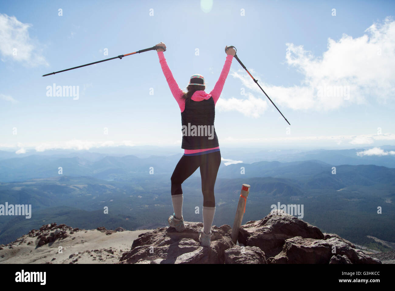 Young woman at mountain top, holding walking poles in air, rear view, Mt. St. Helens, Oregon, USA Stock Photo