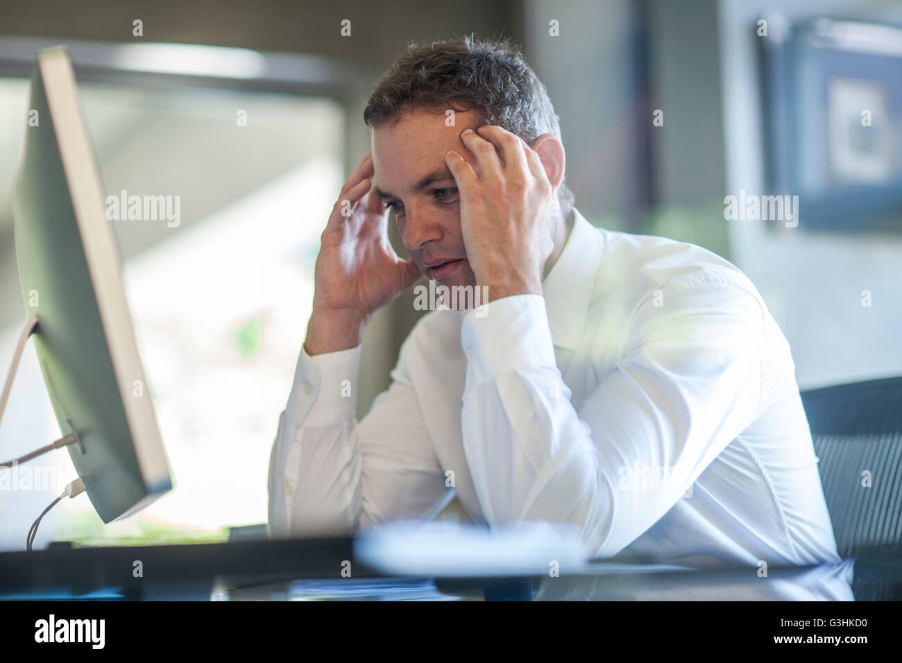 Stressed businessman with hands on forehead at office desk Stock Photo