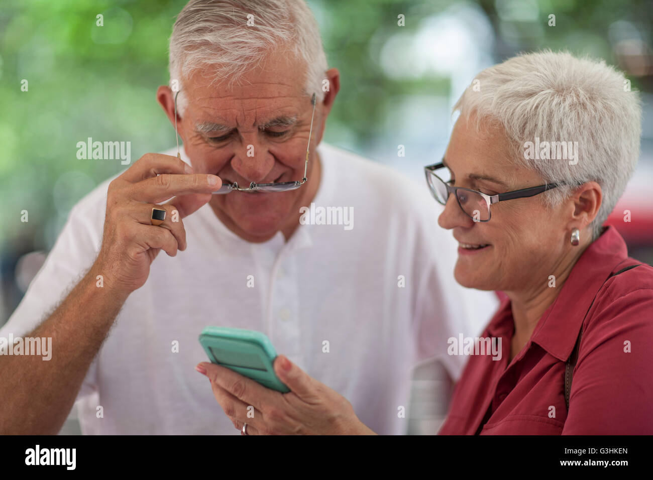 Senior man and woman wearing spectacles reading smartphone in city Stock Photo