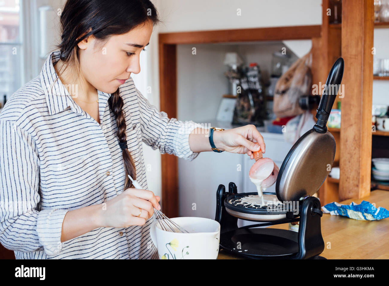 Woman in kitchen adding batter to waffle iron Stock Photo