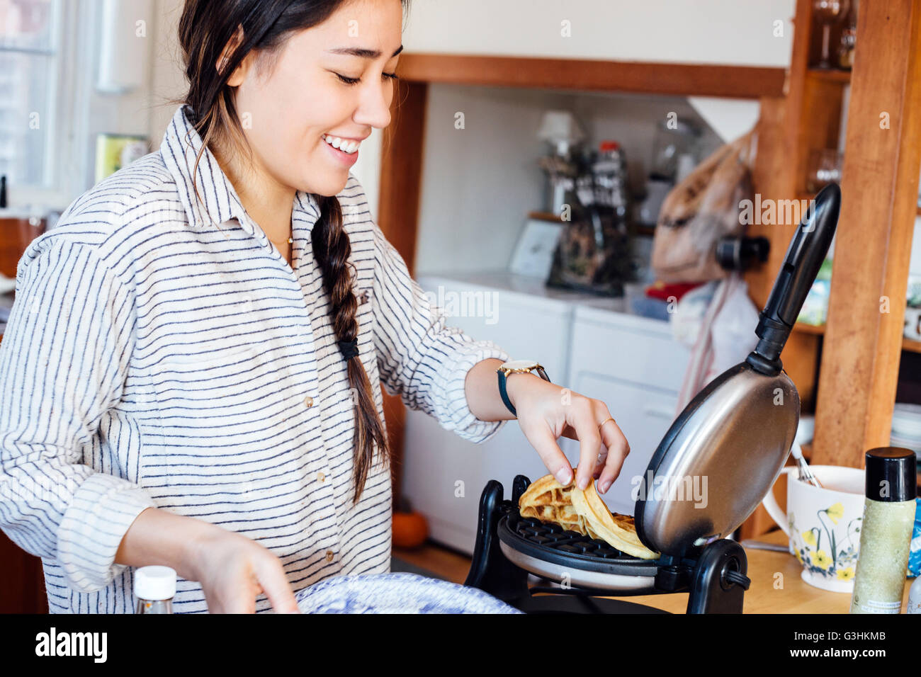 Woman in kitchen removing waffle from waffle iron smiling Stock Photo