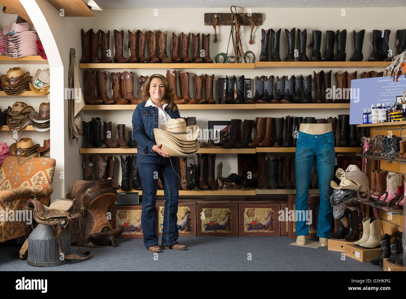 Shop assistant carrying stetsons in front of shelves of boots Stock Photo
