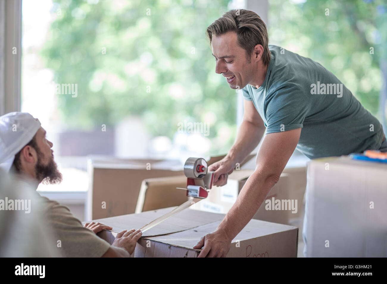 Moving house: two men taping up cardboard box Stock Photo