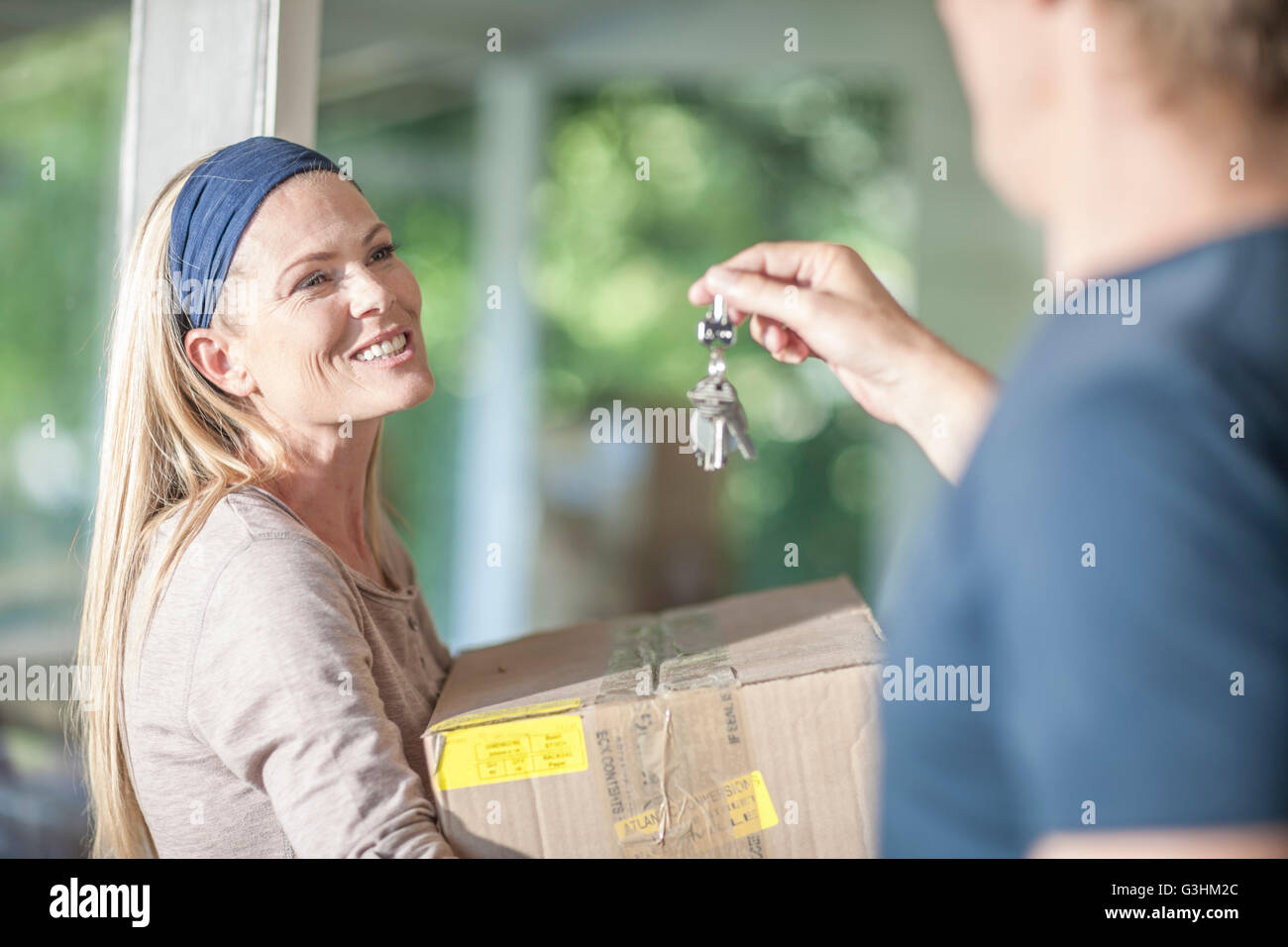 Moving house: woman carrying cardboard box, man holding house keys Stock Photo