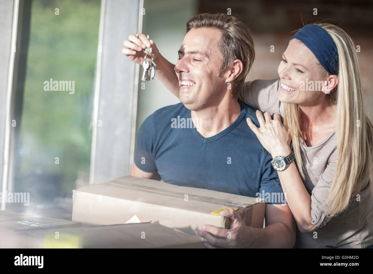 Moving house: man holding cardboard box, woman holding house keys in front of his face Stock Photo