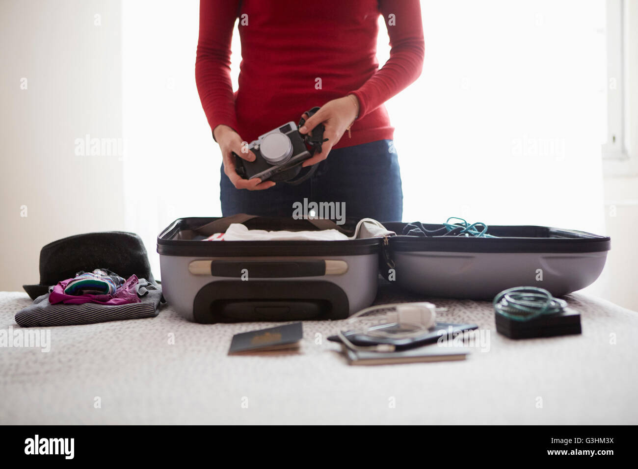 Woman packing suitcase, holding camera, mid section Stock Photo