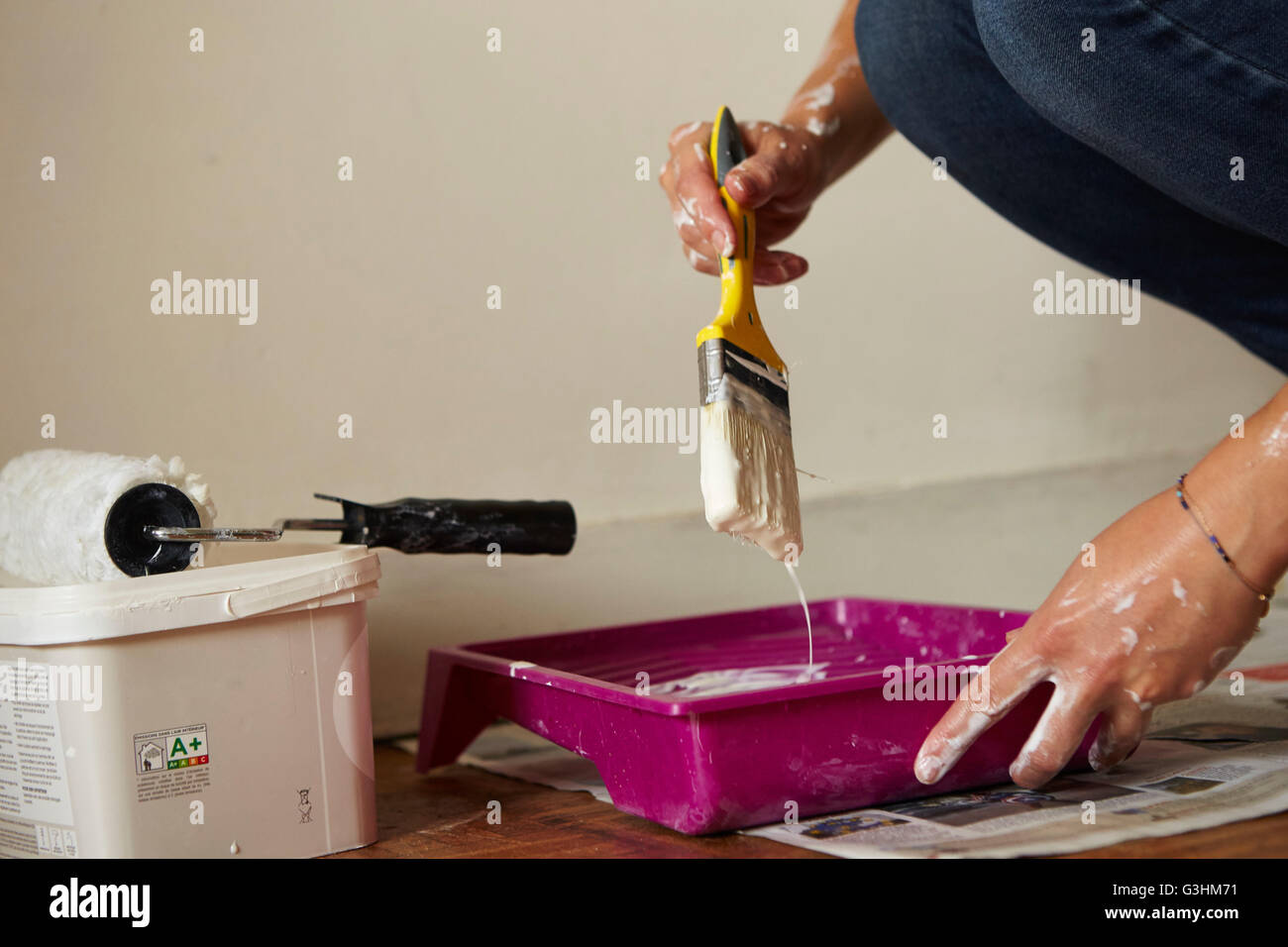 Woman dipping paintbrush into paint tray, close-up, mid section Stock Photo