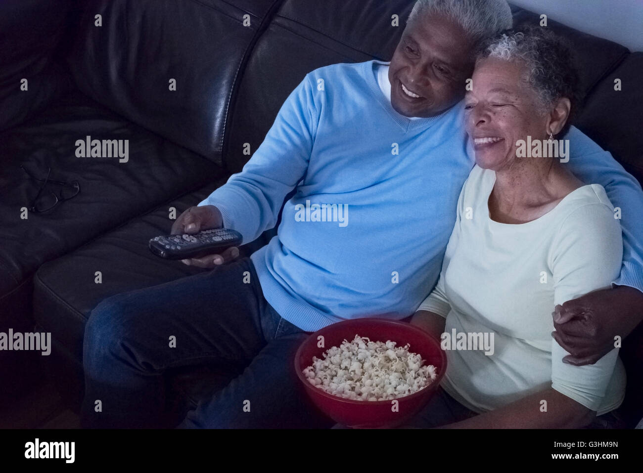 Senior couple sitting on sofa at night, watching television, woman holding bowl of popcorn Stock Photo