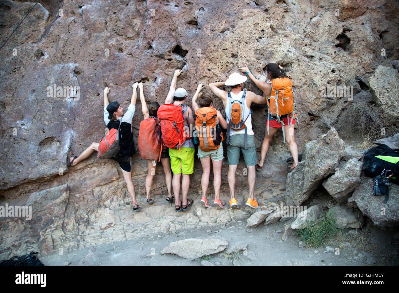 Rear view of group of friends side by side clinging onto rock face Stock Photo