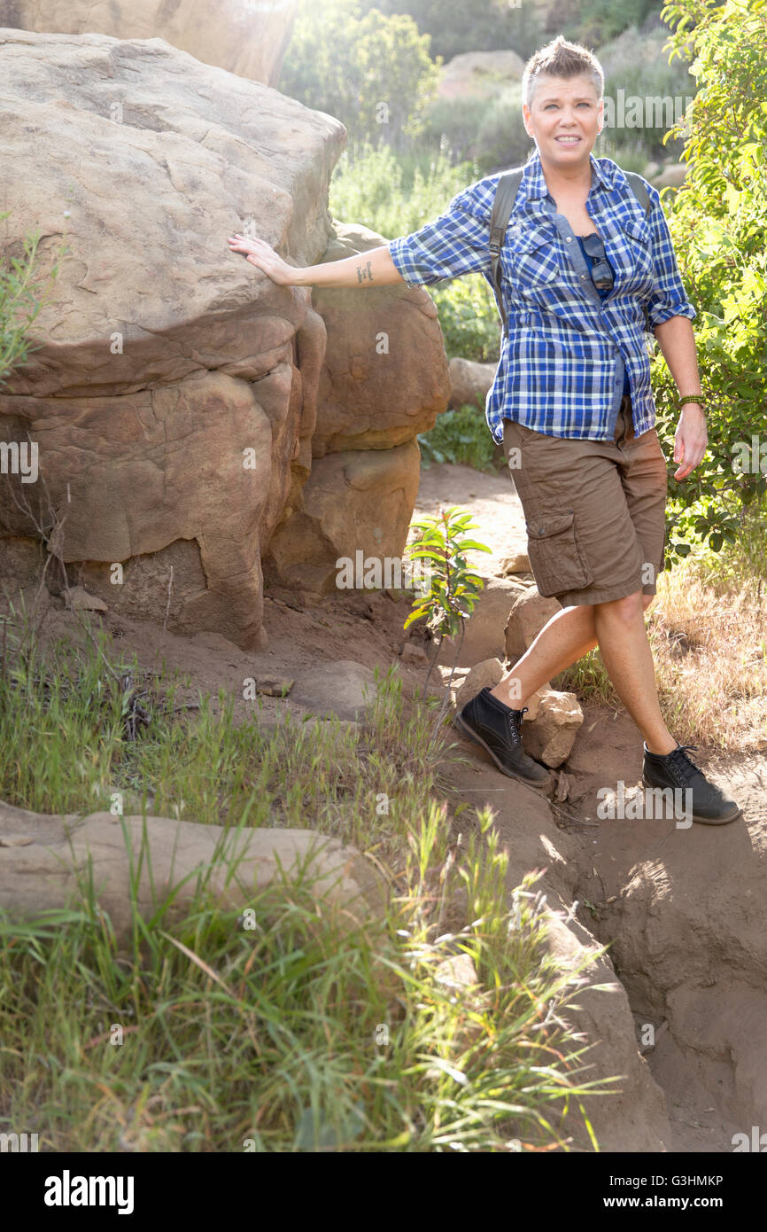 Woman hiker leaning against rock looking at camera smiling Stock Photo