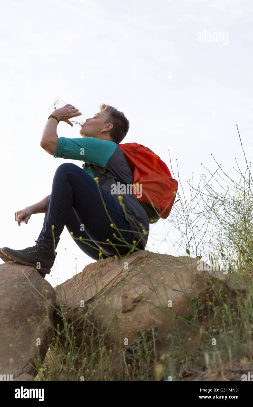 Woman hiker sitting on top of rocks drinking water from bottle Stock Photo