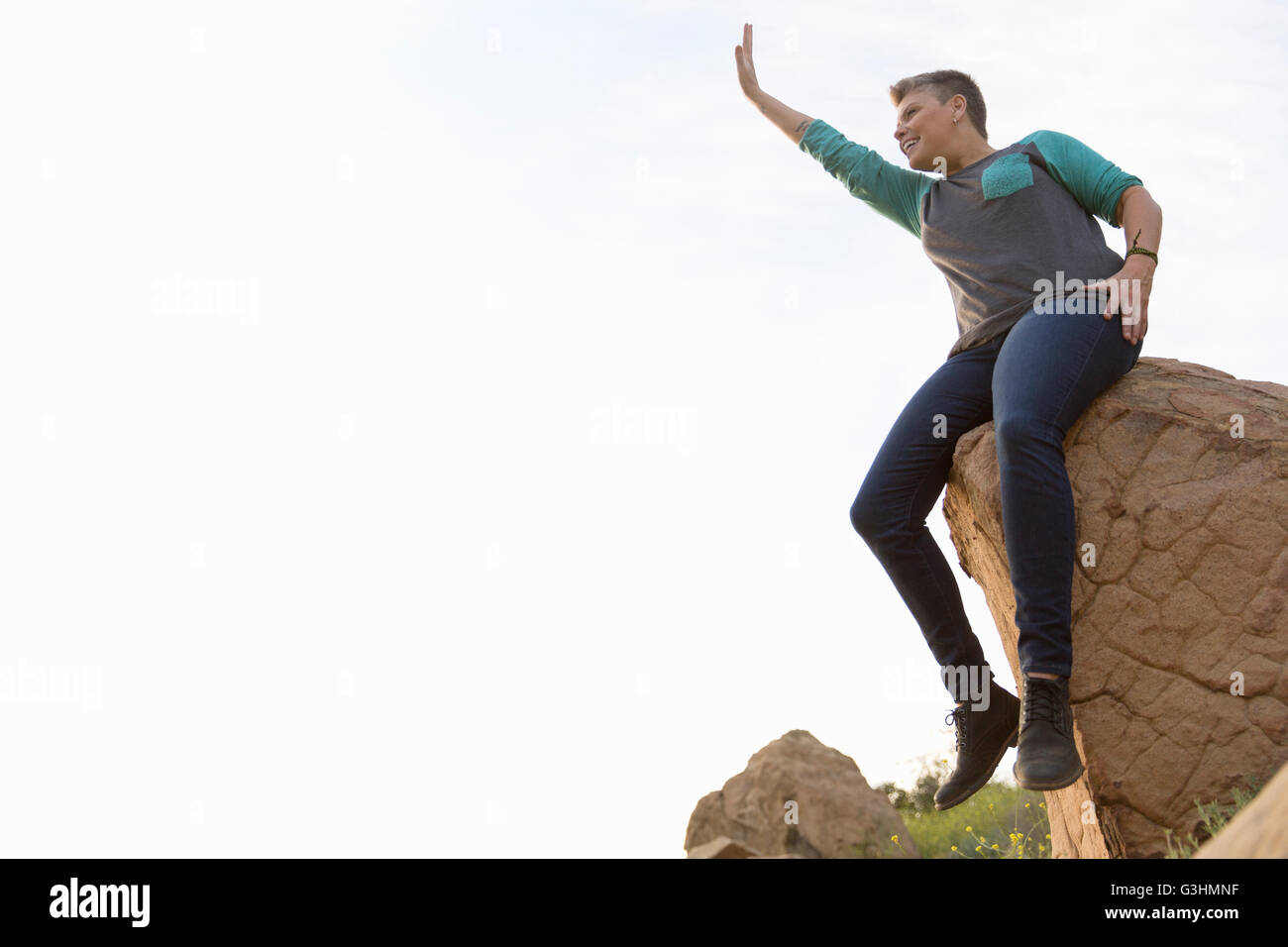 Woman hiker sitting on rocks looking away waving Stock Photo