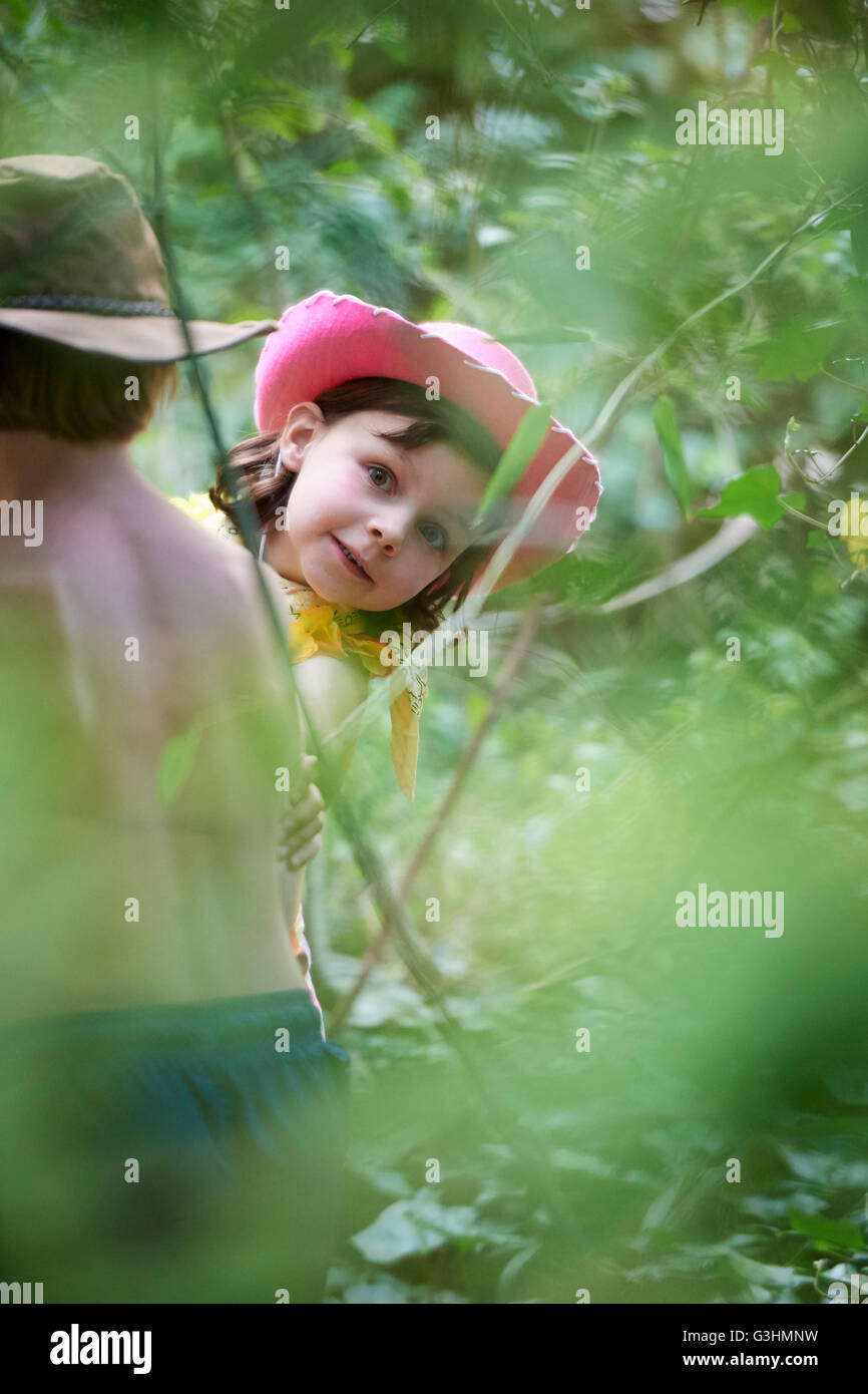 Girl and boy wearing cowboy hats playing in garden bushes Stock Photo